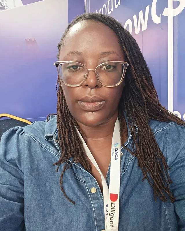Eddah Dena, wearing glasses and a denim shirt, at a conference.